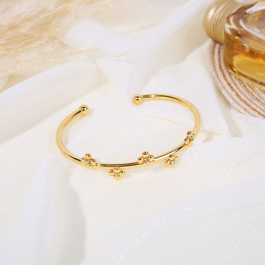 Bracelet jonc doré ouvert avec billes dorées aux extrémités orné de fleurs composées de ronds avec strass