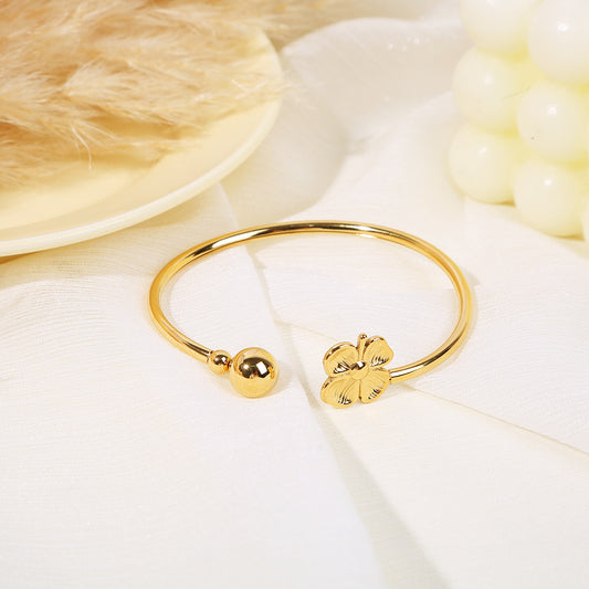 Bracelet jonc doré ouverture avant avec aux extrémités une bille dorée et un trèfle a 4 feuilles