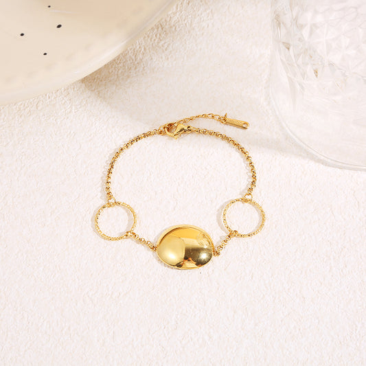 Bracelet chaîne fine dorée avec deux anneaux texturés et pastille centrale bombée finition miroir